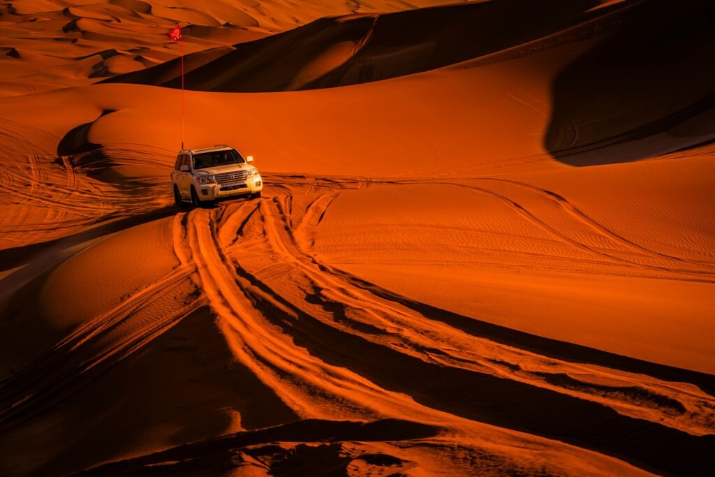 An SUV navigates through expansive sand dunes at sunset, creating a thrilling adventure scene.