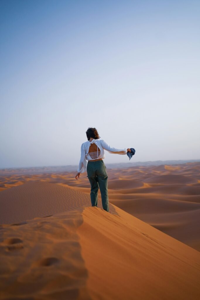 A woman stands alone on a desert dune, capturing the vastness of the arid landscape under a clear sky.
