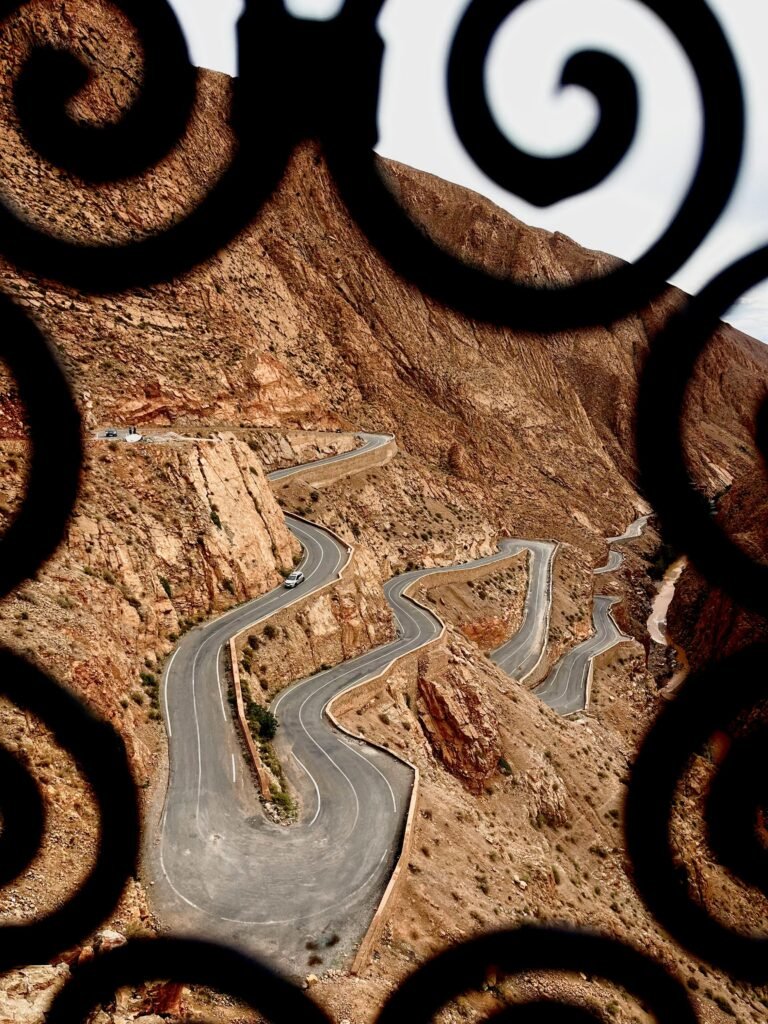 Scenic view of a winding road through the Atlas Mountains framed by ornate ironwork.