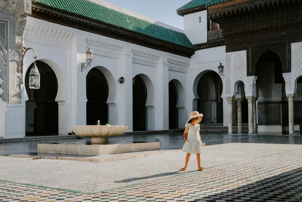 A child explores the historic Al-Qarawiyyin Mosque courtyard in Fes, Morocco on a sunny day.