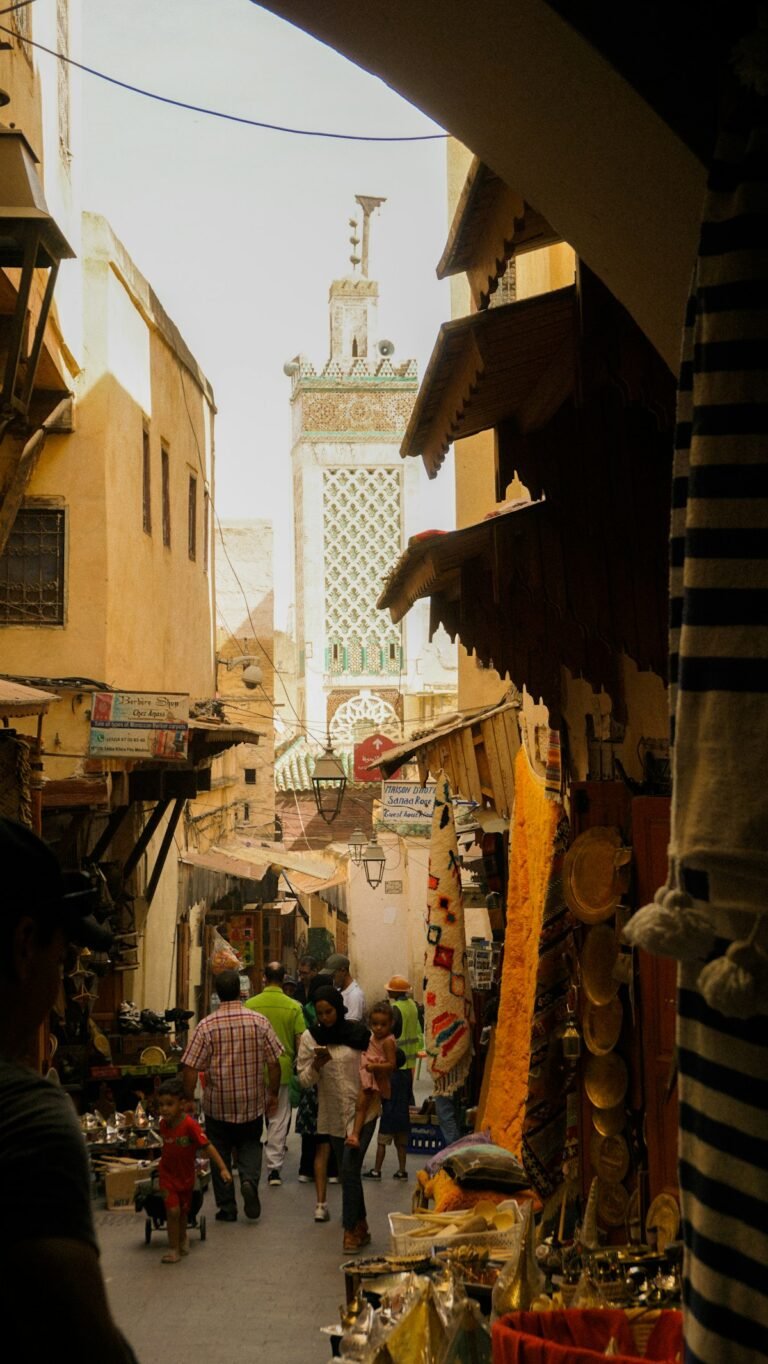 A bustling medina alley in Fes, Morocco, with a minaret in the background