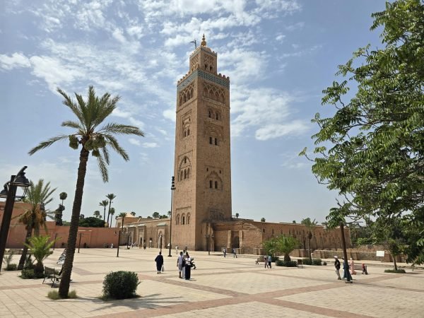 Koutoubia Mosque's majestic minaret stands tall in Marrakesh, Morocco, with people strolling below.