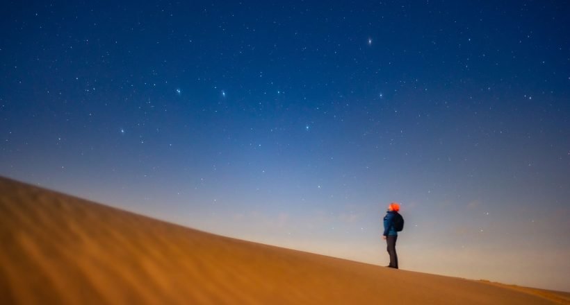 A traveler stargazing from a Sahara dune under a clear night sky in Morocco
